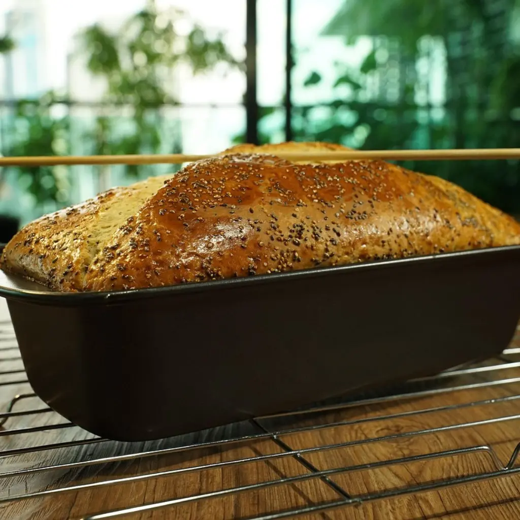 Freshly baked banana bread loaf topped with poppy seeds in a loaf pan on a cooling rack